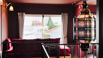 A room with a view of a building through a window, a hanging lantern, and a red sofa.