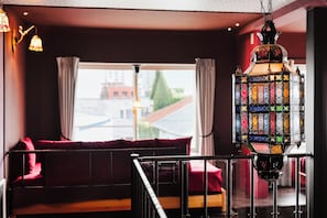A room with a view of a building through a window, a hanging lantern, and a red sofa. - THE BEEHIVE AIOI (Otaru)