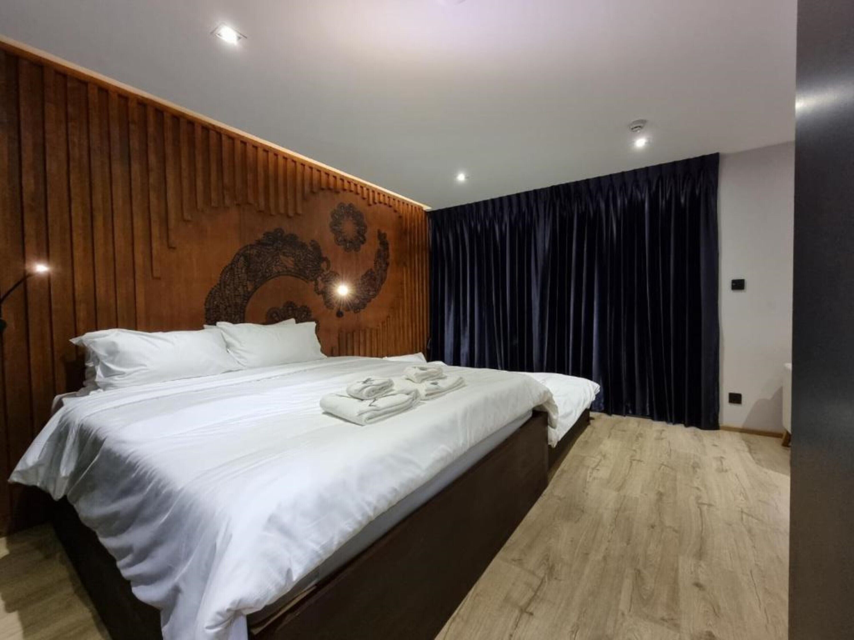A modern bedroom with a wooden headboard, a large bed with white linens, and a dark blue curtain.