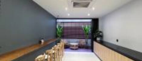 A modern interior with a long counter and bar stools, a seating area with a sofa, and a large window with plants.