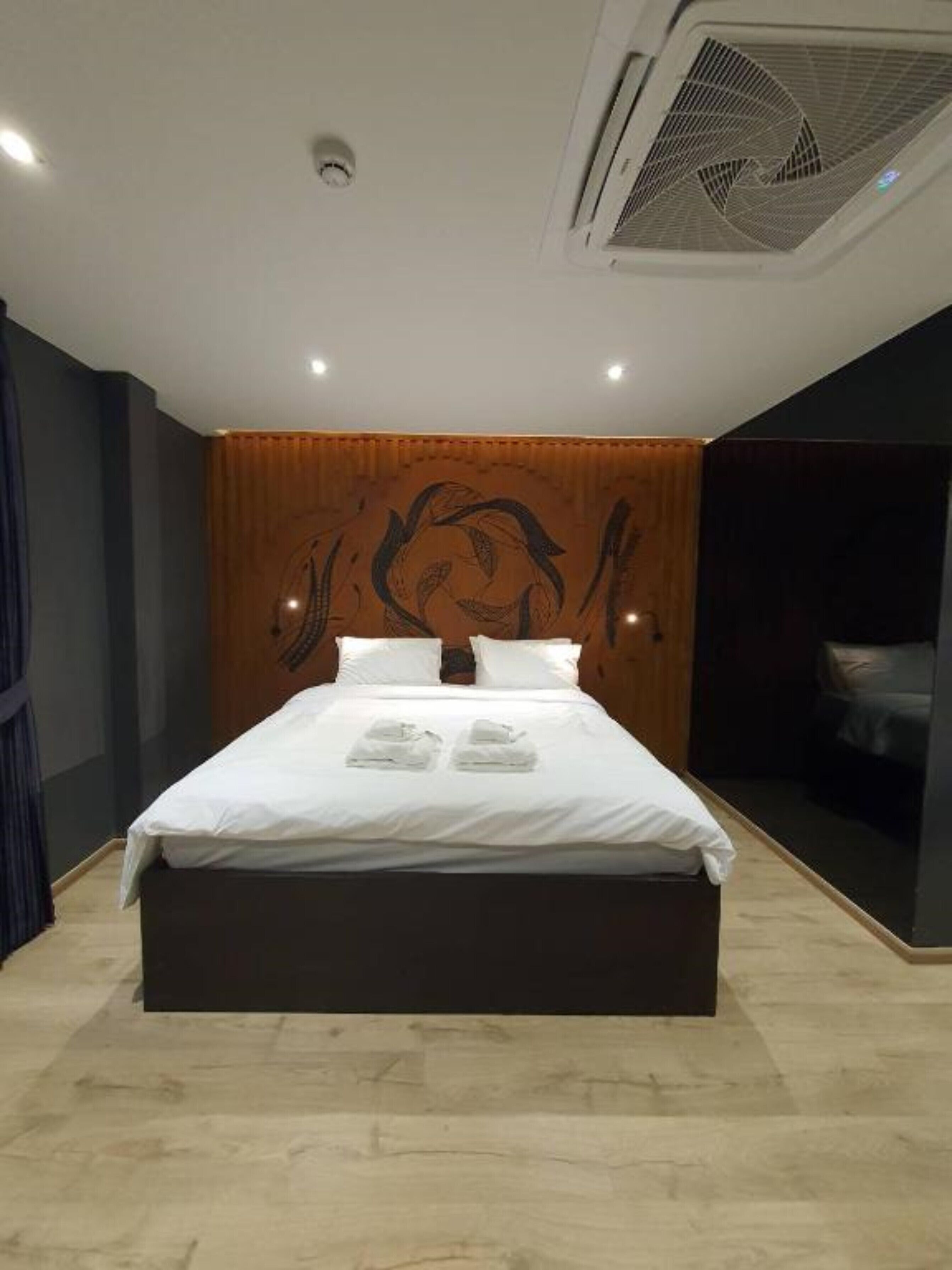 Ein modernes Hotelzimmer mit einem großen Bett, einem Holzkopfende mit dekorativer Verkleidung und einem Deckenventilator.