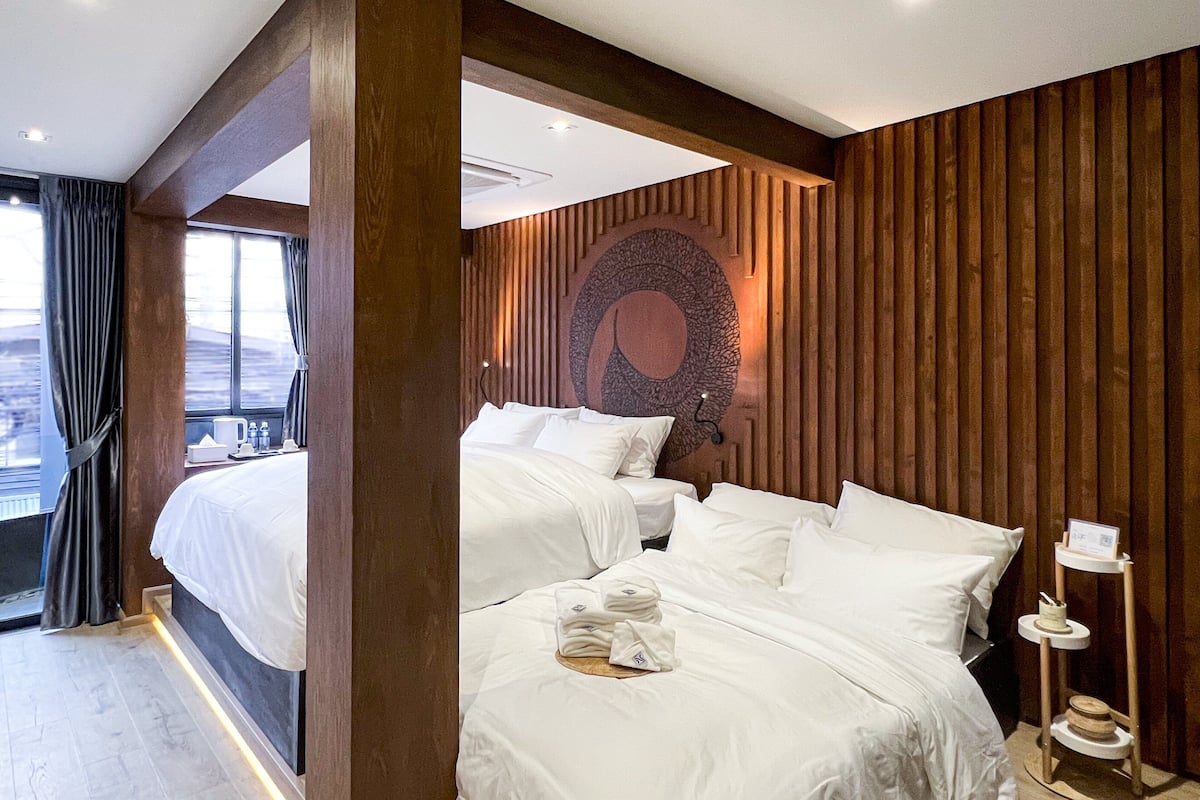 A hotel room with two beds, a wooden accent wall, and a view of the city.