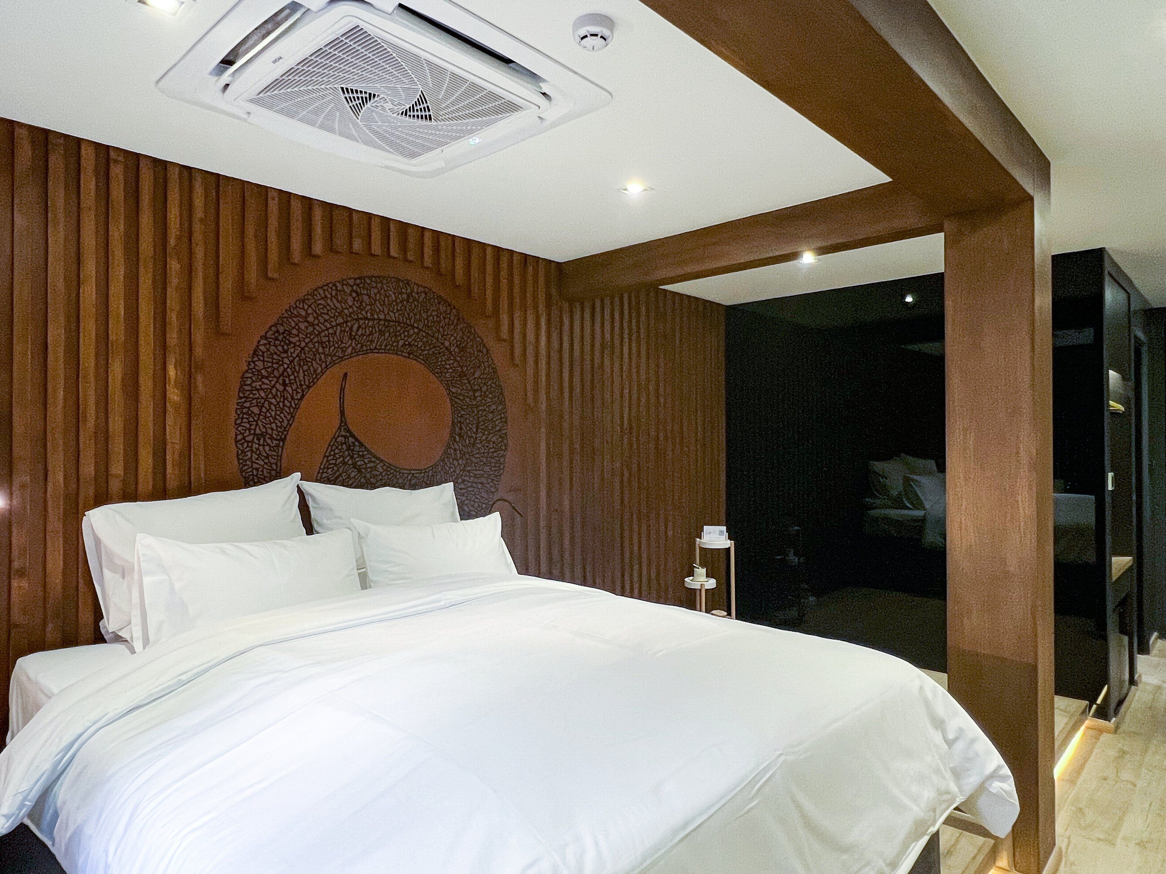 A modern bedroom with a large bed, wooden paneling, a circular wall decoration, and a visible bathroom.