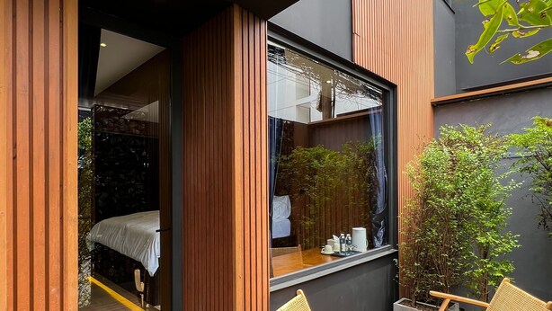 A modern outdoor seating area with wicker chairs, a glass door leading to a bedroom, and a view of a garden. - The Nhorm Hotel Ratchada (Bangkok)