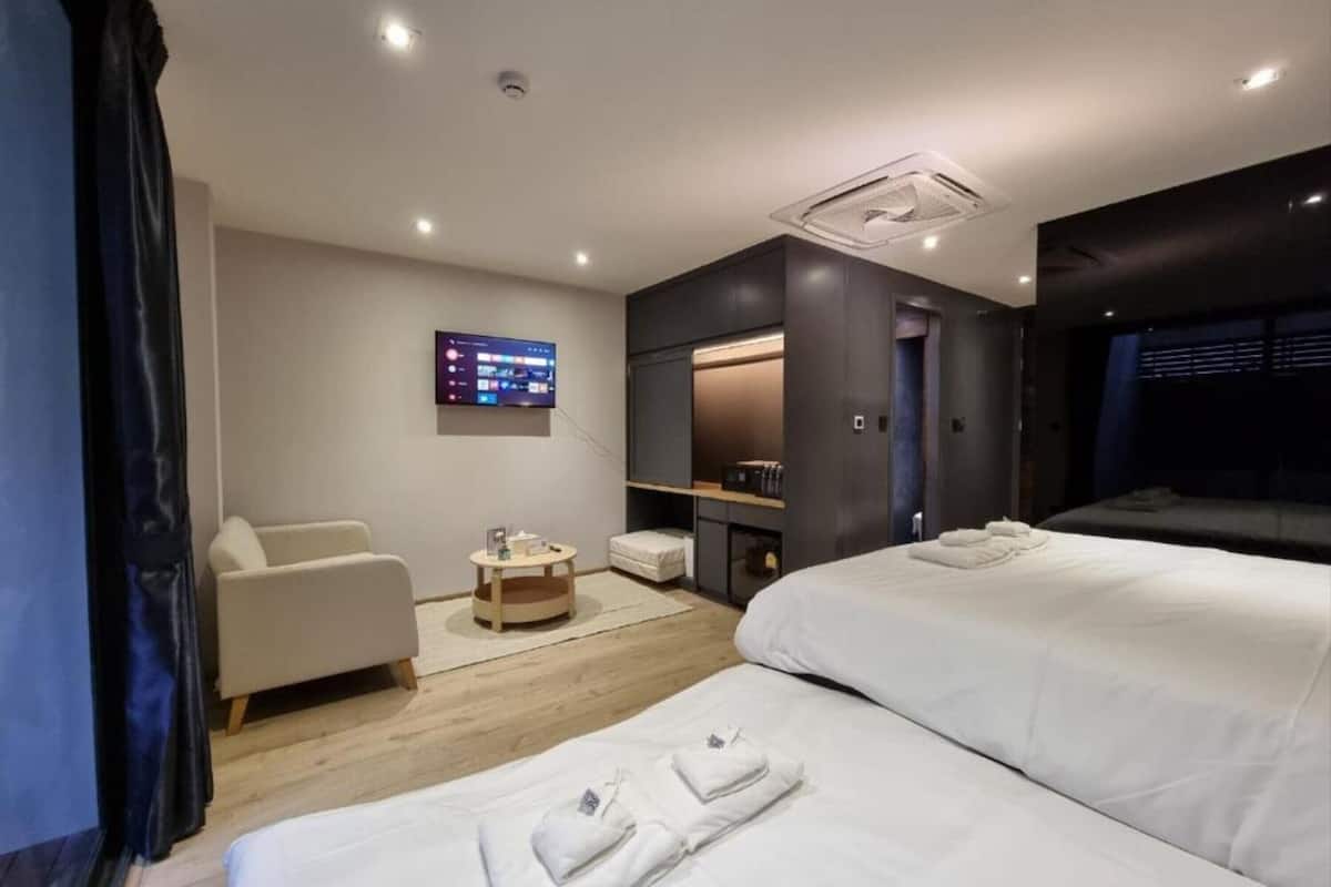 A modern hotel room with two beds, a seating area, a TV, and a small table.