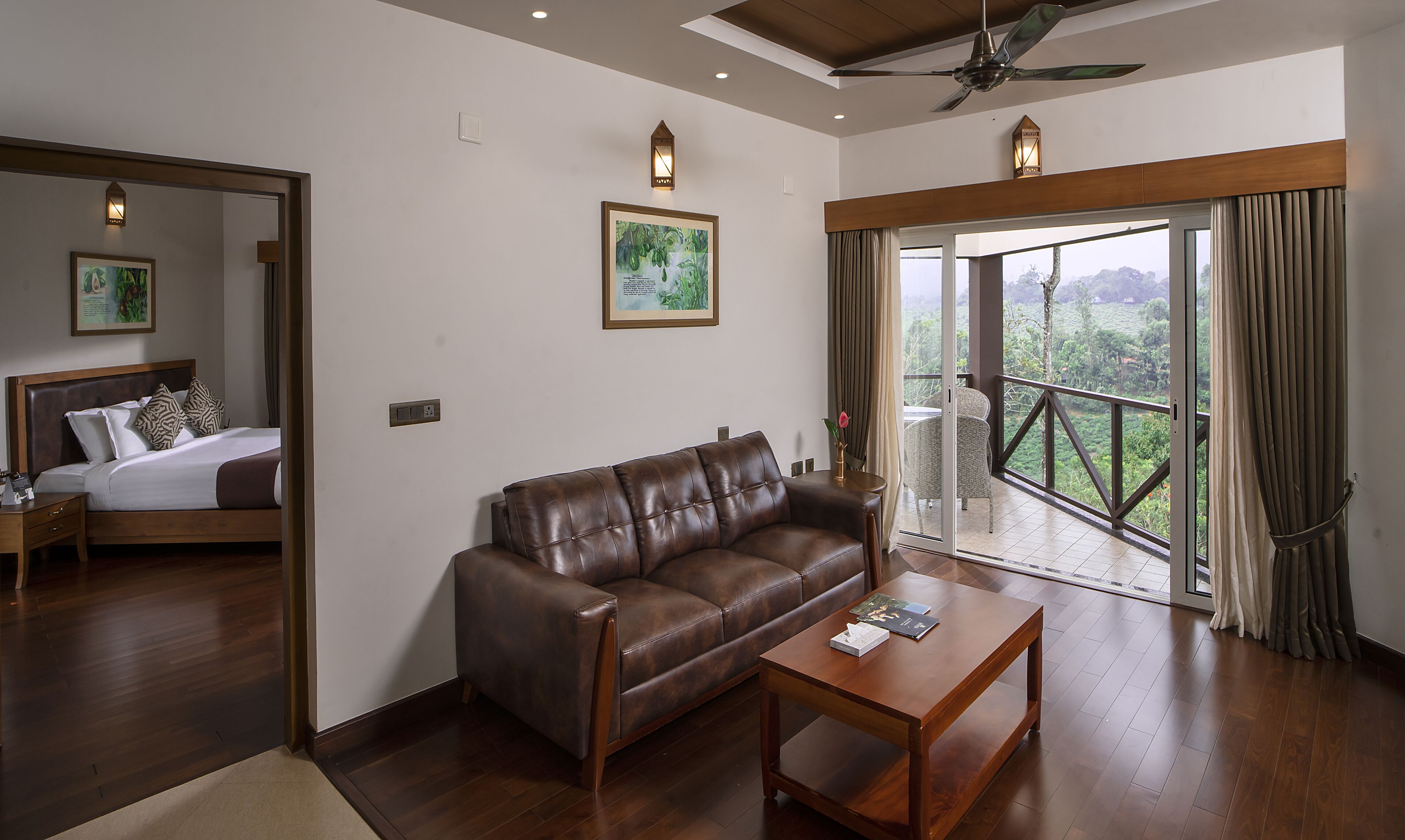 A hotel room with a bed, a leather sofa, a wooden coffee table, and a balcony with a view of greenery.