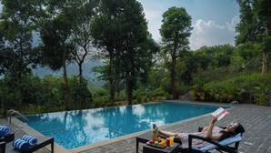 Ein Poolbereich mit Liegestuhl, Tisch mit Obstplatte und Blick auf eine natürliche Landschaft.