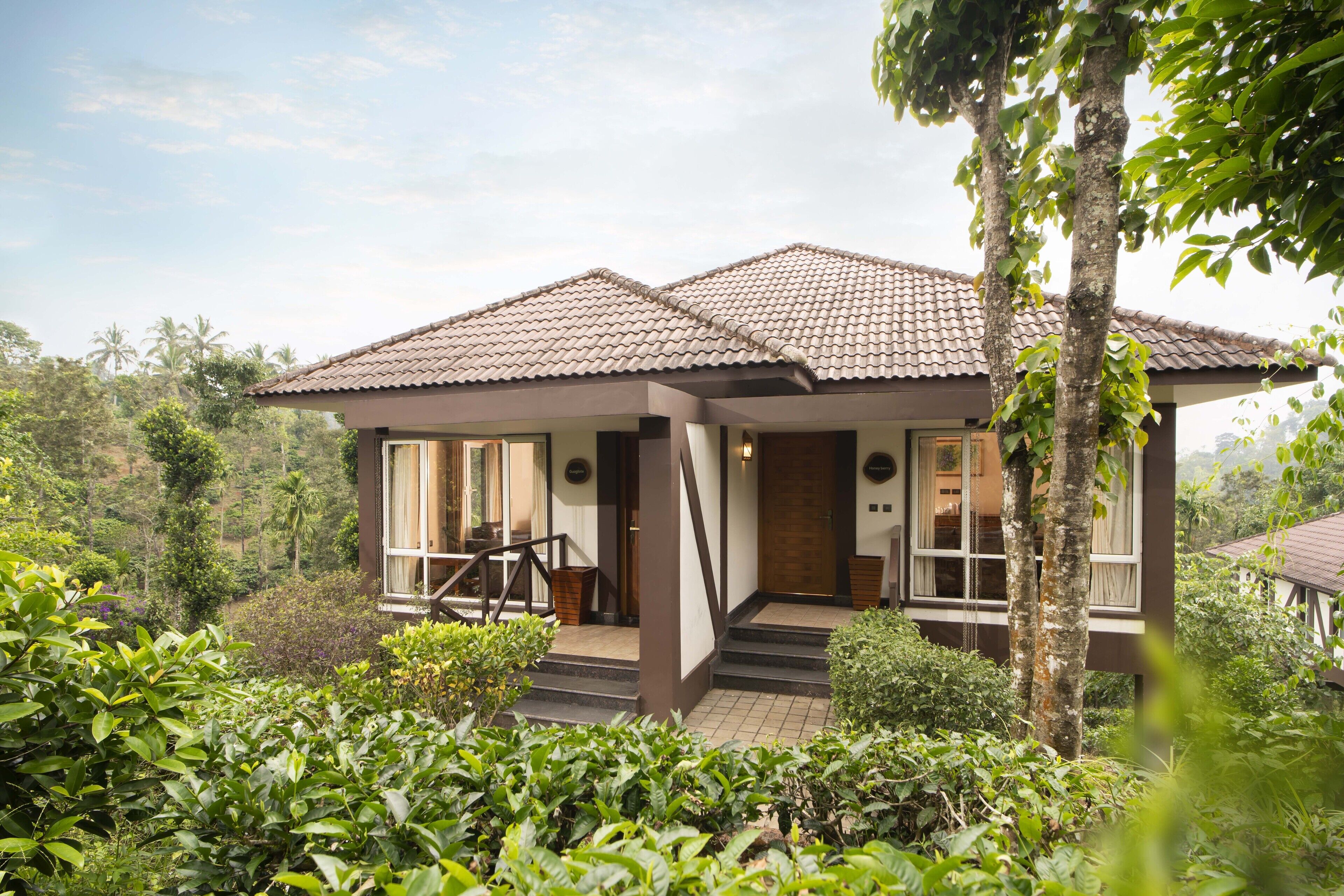 A two-story house with a tiled roof, surrounded by lush greenery and palm trees.