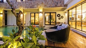 Zona moderna de piscina interior con pared de piedra, mobiliario de mimbre y vistas al interior.