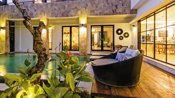 A modern indoor pool area with a stone wall, wicker furniture, and a view of the interior.