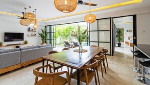 A modern living room with a wooden dining table, grey sofa, and wicker pendant lights.
