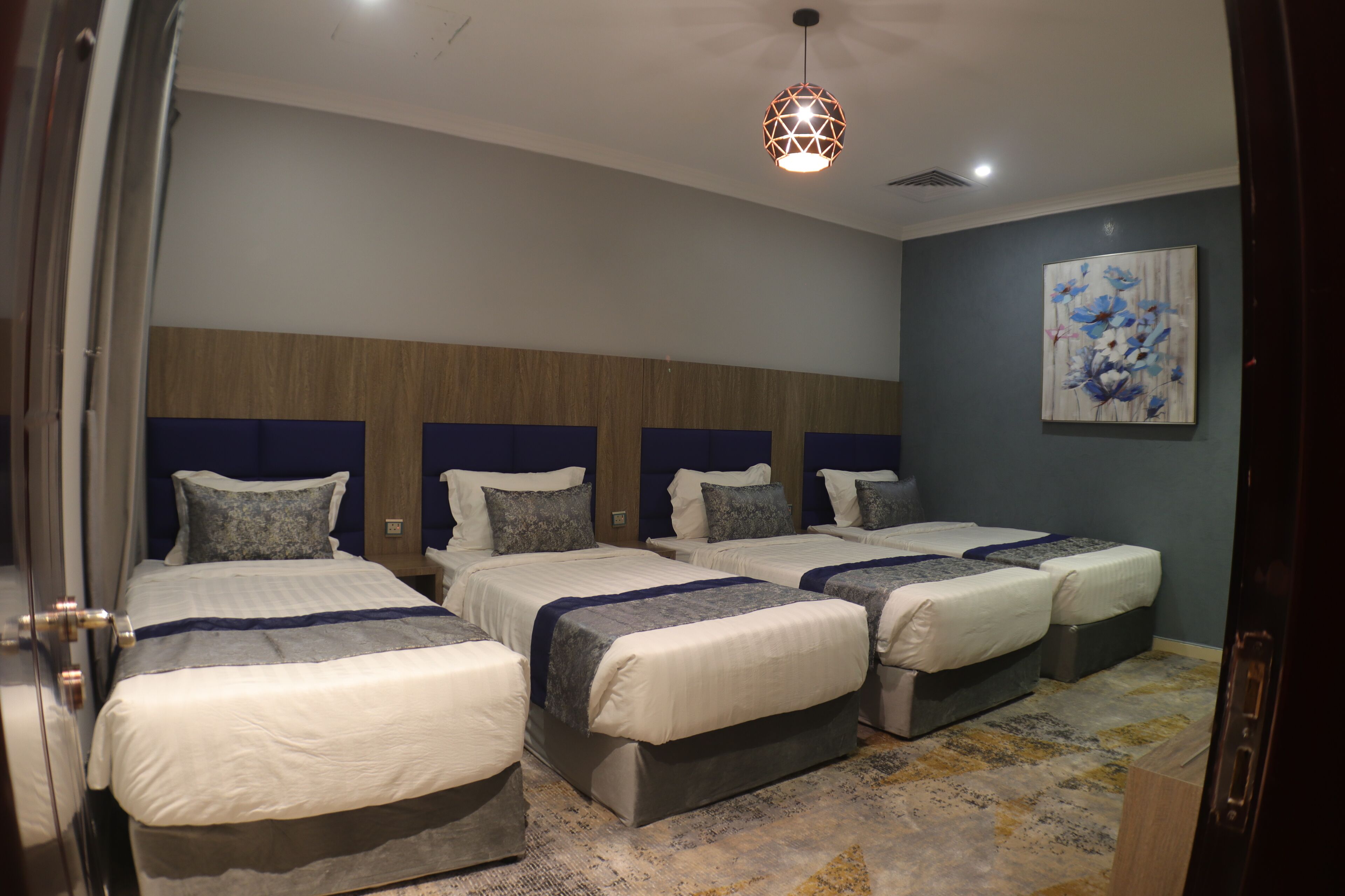 Ein Hotelzimmer mit drei Betten, einem hölzernen Kopfteil, einer blauen Wand und einem Blumenbild.