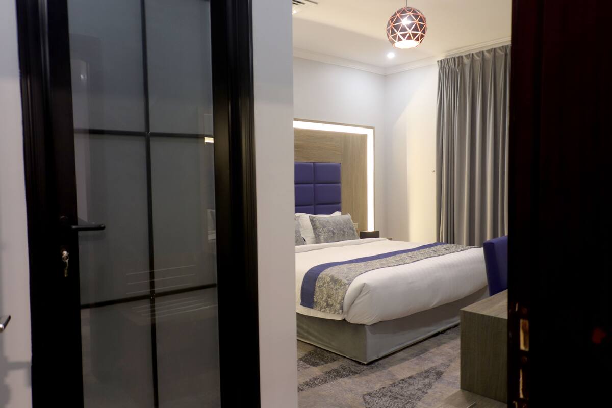 A modern hotel room with a large bed, a bedside table, a nightstand, and a built-in headboard.