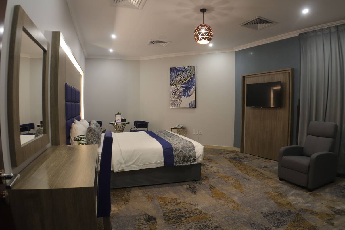 A modern hotel room with a large bed, a desk, a chair, a TV, and a large mirror.
