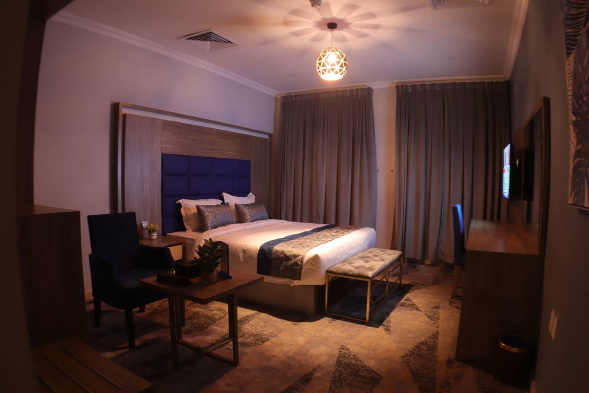A hotel room with a bed, a desk, a chair, a TV, and a ceiling light fixture.