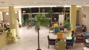 A spacious lobby with a palm tree, seating areas, and a reception desk.