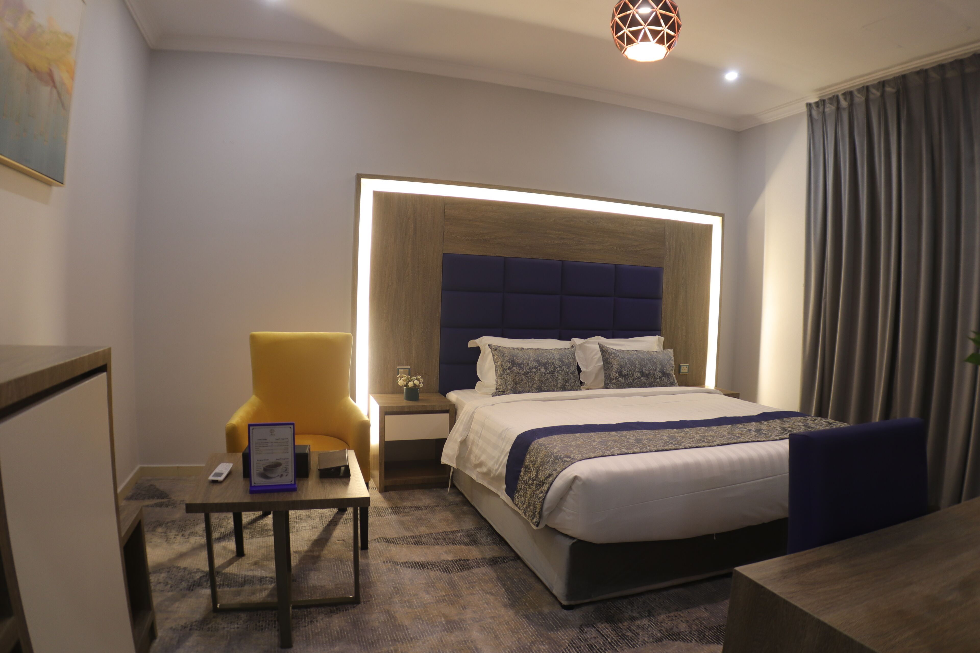A modern hotel room with a large bed, a bedside table, a chair, and a small desk.