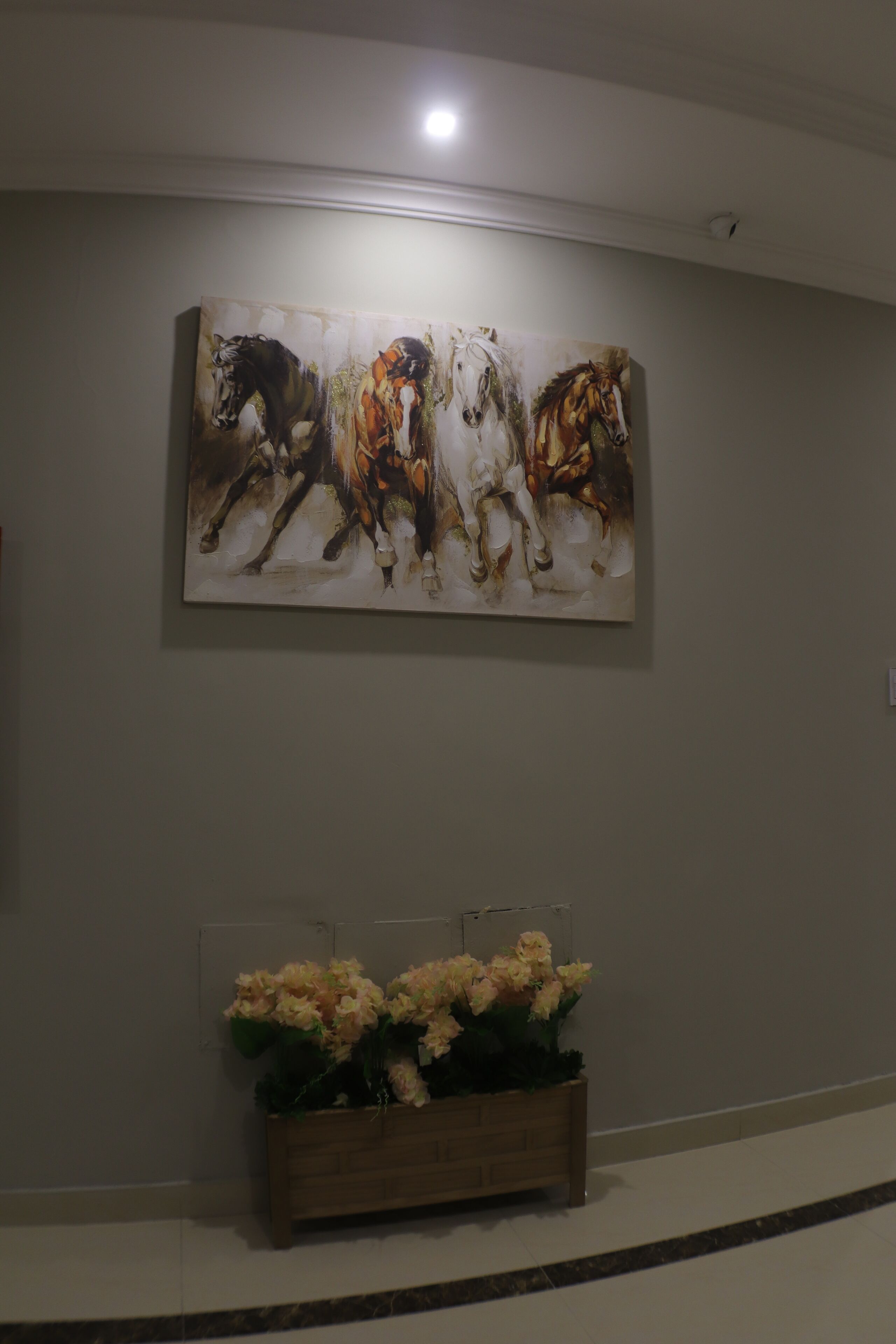 Un pasillo con un cuadro abstracto grande de caballos en la pared y una maceta de madera con flores.