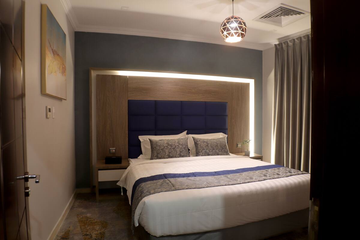 A modern hotel room with a large bed, a wooden headboard, a bedside table, and a nightstand.
