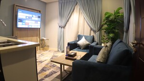 A living room with a sofa, a coffee table, a TV mounted on the wall, and a potted plant.