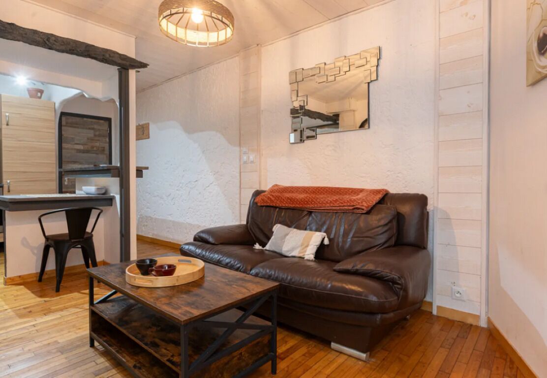 Un salon chaleureux avec un canapé en cuir, une table basse en bois et un coin repas comprenant une chaise et une petite table.