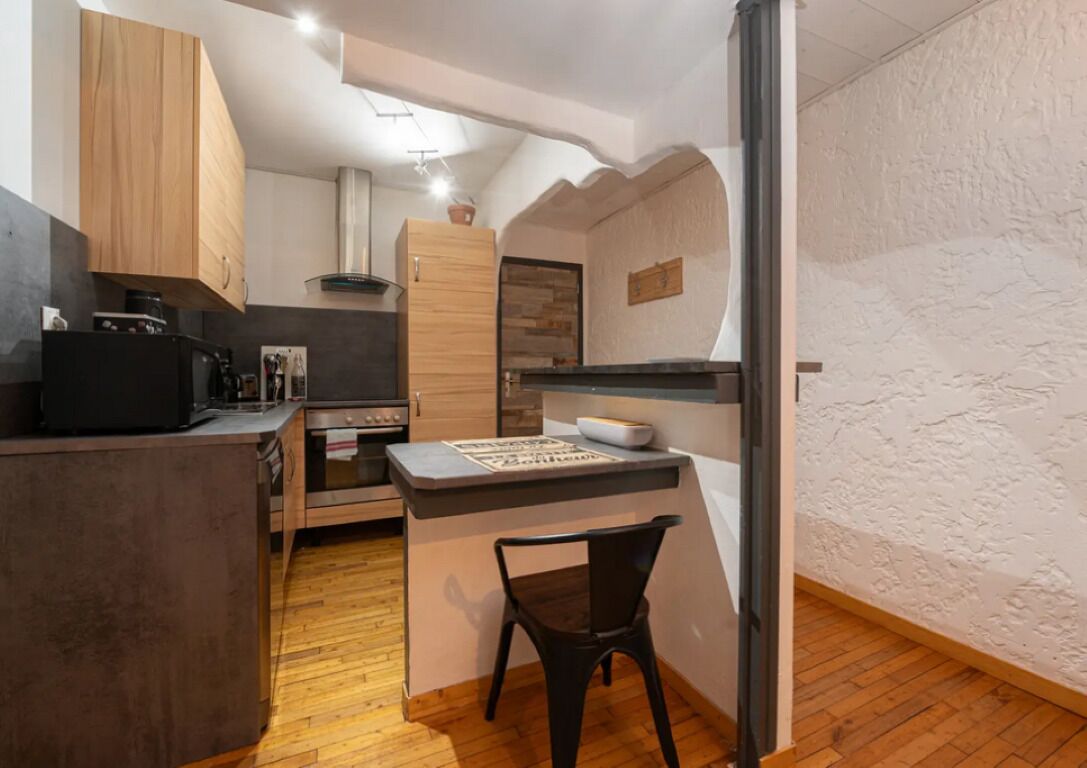 A compact kitchen with wooden cabinets, a built-in oven, and a small island with a chair.