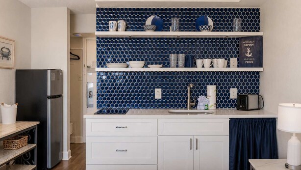 Eine kleine Küche mit blauer, sechseckiger Fliesenrückwand, weißen Schränken, einem schwarzen Kühlschrank und einem Spülbecken mit Handtuchhalter.