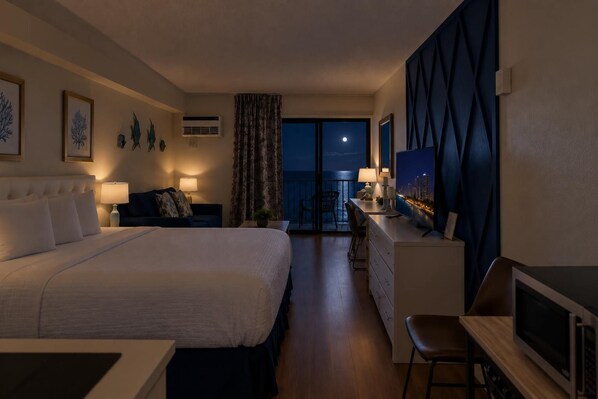 A hotel room with a bed, a desk, a TV, and a view of the night sky.