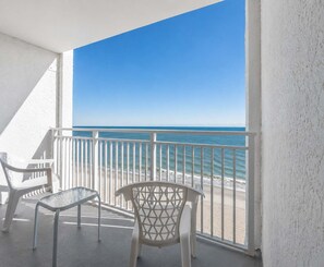 A balcony with a view of the sea, white chairs, and a white railing.