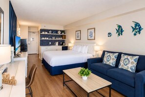 A hotel room with a bed, a sofa, a desk with a computer, a TV, and a kitchenette.