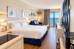 A hotel room with a bed, a desk, a chair, a small table, and a view of the sea.