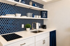 A kitchen with a blue hexagonal tile backsplash, white cabinets, a stainless steel sink, and a countertop with various items including a toaster and a potted plant.