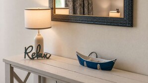 Ein weißer Tisch mit einer Lampe, einem dekorativen Schild und einem blauen, schiffartigen Behälter.