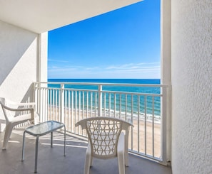 Un balcon avec vue sur l’océan, deux chaises en plastique blanches et une table en verre.