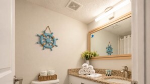 Ein Badezimmer mit Toilette, Waschbecken und Spiegel. Handtücher und Toilettenartikel liegen auf der Ablagefläche.