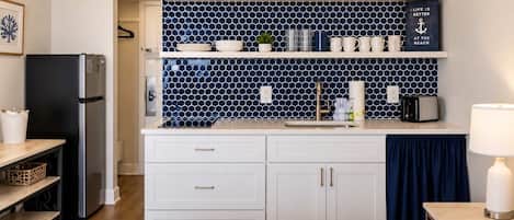 A compact kitchen with white cabinets, a black refrigerator, and a blue tiled backsplash.