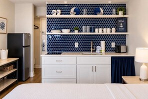 A compact kitchen with white cabinets, a black refrigerator, and a blue tiled backsplash.