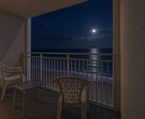 A balcony with a view of the ocean at night, featuring a chair and a small table.