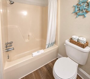 Une salle de bain avec une baignoire, des toilettes et une décoration représentant un gouvernail de bateau sur le mur.