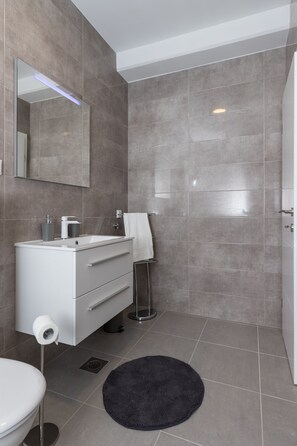 Un bagno moderno con un mobile lavabo bianco, uno specchio, un porta asciugamani e una doccia.