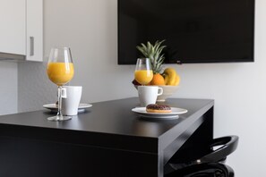 Colazione con due bicchieri di succo d'arancia, una tazza bianca, un piattino con un donut al cioccolato e una ciotola di frutta, tra cui ananas e banane.