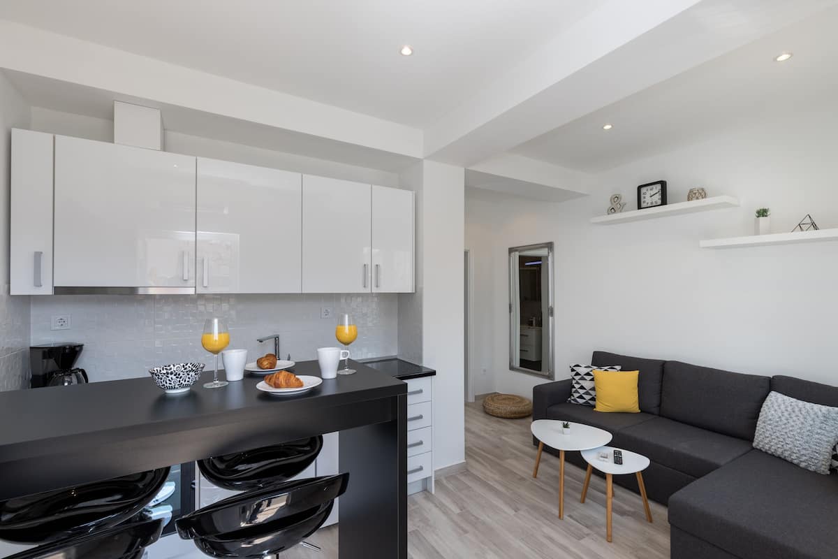 A modern kitchen with white cabinets, a black countertop, and a dining area with a black chair and a small white table.
