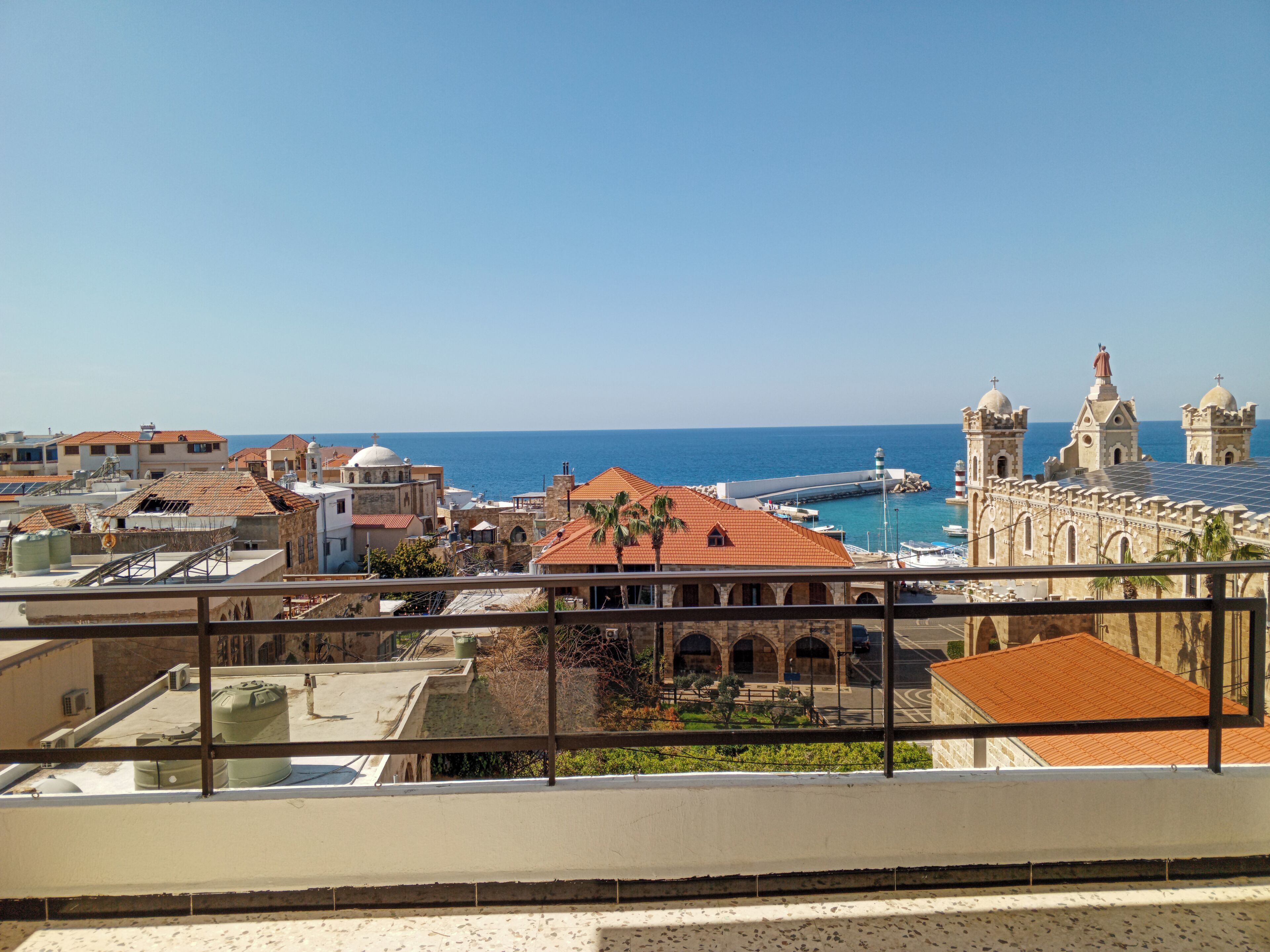 Paisatge urbà costaner amb arquitectura històrica, un port esportiu i una vista clara del mar.