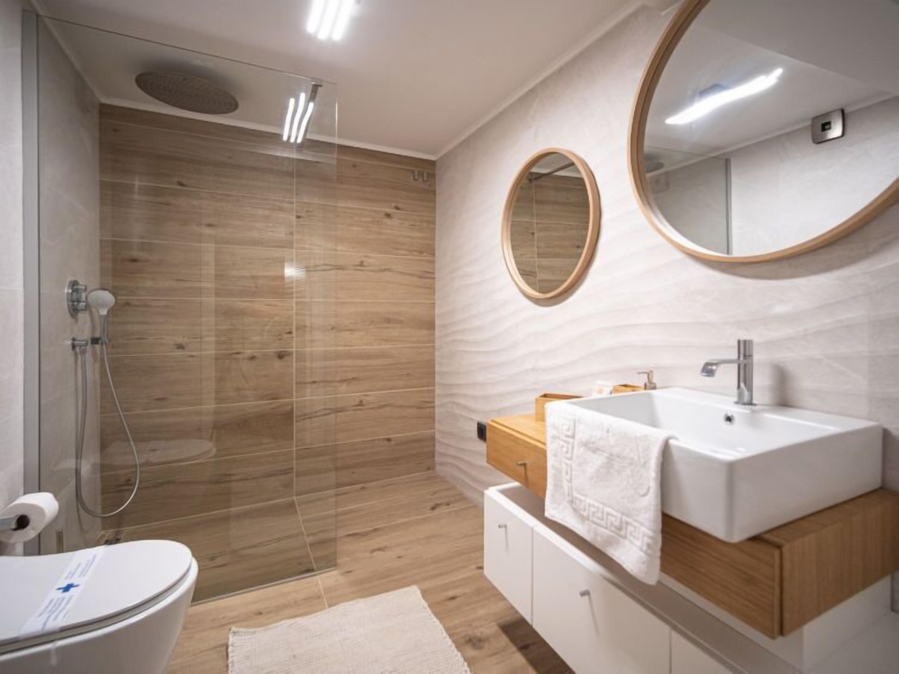 Une salle de bain moderne avec une douche à l’italienne en verre, un lavabo blanc et un meuble-lavabo en bois.