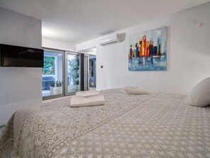 Un dormitorio con una colcha estampada, un televisor de pantalla plana en la pared y un cuadro de edificios coloridos.