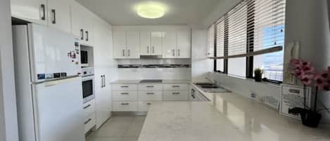 A modern kitchen with white cabinetry, a central island, and a window with blinds.