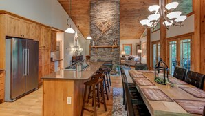 Una cocina amplia con armarios de madera, una isla grande con taburetes, una chimenea de piedra y un comedor con una mesa larga y sillas.
