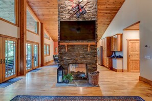 Cozy living space with a stone fireplace, flat-screen TV, and kitchen area.