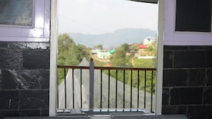 Un balcon donnant sur un bâtiment verdoyant et sur des collines à l’horizon.