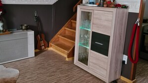 A room with a wooden staircase, a cabinet with glass doors, a guitar, a lantern, and a red leash. - Idyllic vacation home in the middle of nature (Neunkirchen)